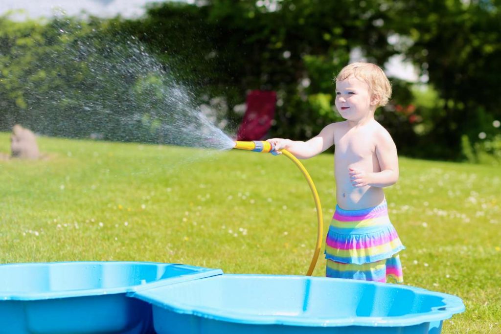 dítě stříka vodu z hadice do bazénku